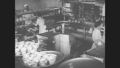 1940s: Busy restaurant kitchen. Cook plates food and hands it to waitress. Cook Stock Footage