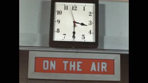 1940s: Clock on wall above "On the Air" sign. Man in radio studio gives signal Stock Footage 195119344