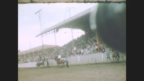 1940s: Cowboys race horses down the track at a rodeo. Faces of audience members Stock Footage