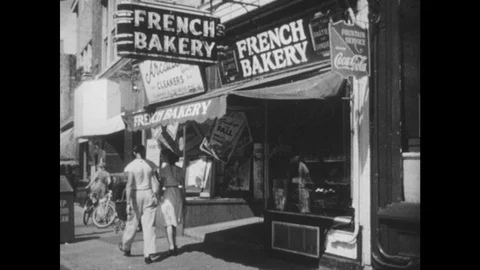 1940s: Exterior of bakery. Bread in window. Man repairing shoes. Woman and girl Stock Footage 88304782