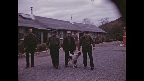 1940s: Four men walk in front of long building, man pets pointer dog, dog wags Stock Footage 85198639