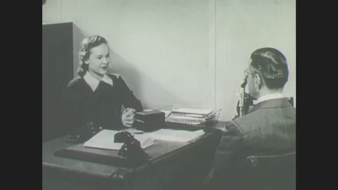 1940s: Girl and man sit at desk in office. Girl and man talk to each other. Stock Footage