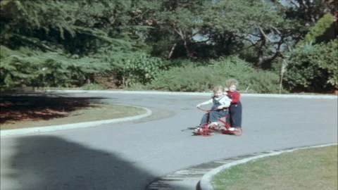 1940s: Girls ride tricycle around driveway. Woman walks on driveway. Woman sets Stock Footage