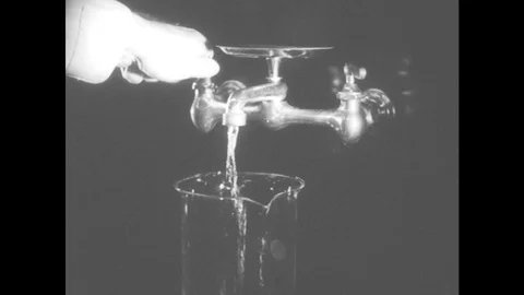 1940s: Hand turns on faucet. Water runs into beaker. Water fills beaker Stock Footage