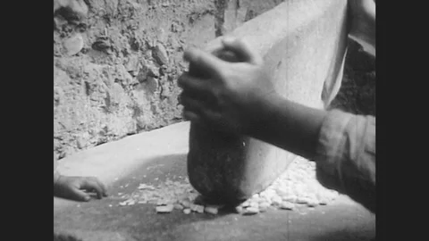1940s: hands grind corn with a large stone. man pulls bread out of wood fire Video stock 79975227
