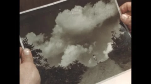 1940s: Hands hold a black and white photograph of clouds. Man operates a Stock Footage 276773123