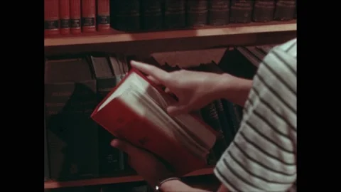 1940s: Hands take book from shelf, zoom out, boys looking through book, walk to Stock Footage 232182270