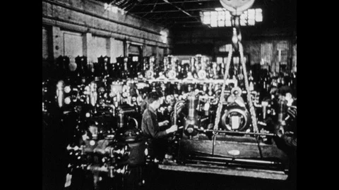 1940s: Inside factory, large machine is lifted by crane and assisted by two men. Stock Footage 106415434