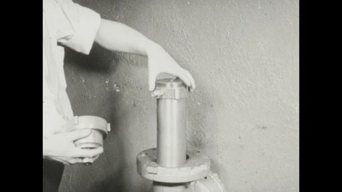 1940s: Lab, man places test chamber canister into pipe, tightens with long 動画素材 116861227