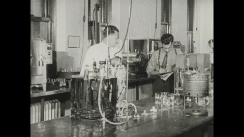 1940s: Lab, men work, examine equipment, take notes. Man turns knob, lights Stock Footage 116861422