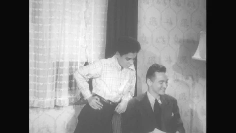 1940s: Man Sits In Chair, Boy Leans On Back, Man Hands Boy Check, Boy Smiles And Stock Footage