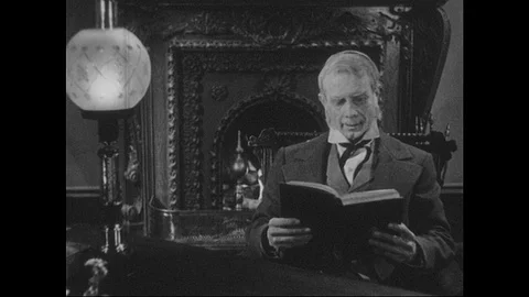 1940s: Man sits at desk, in front of fire, reads book. Man closes book, sets Stock Footage 90828045