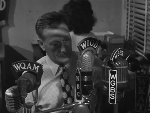 1940s: Man sits down in front of variety of radio mics Stock Footage 229730693