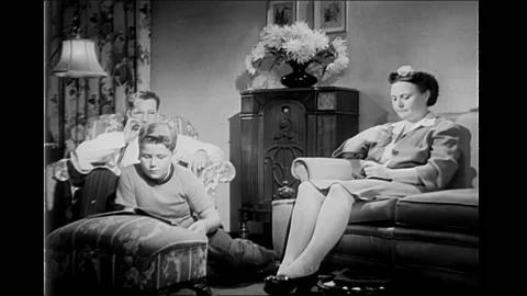 1940s: Man turning knobs on machine. Man smoking pipe. Family sitting in living 库存影片 166398089