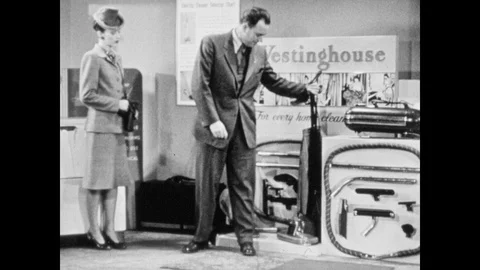 1940s: Salesman displays upright vacuum cleaner to woman. Salesman and woman Stock Footage 90524061