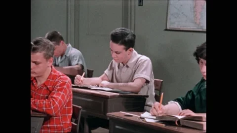 1940s: Students sit in class, study at desks. Boy looks back at clock. Clock on Video stock 220379890