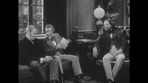 1940s: Two men sit on couch, talk. Man sits in nearby chair, listens. Man hands Stock Footage 90828027