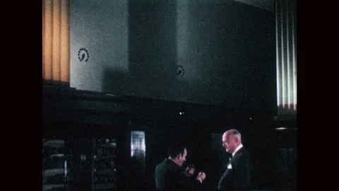 1940s: Two men speak in large, dark room. One man smokes a pipe; the other man Stock Footage 83924879