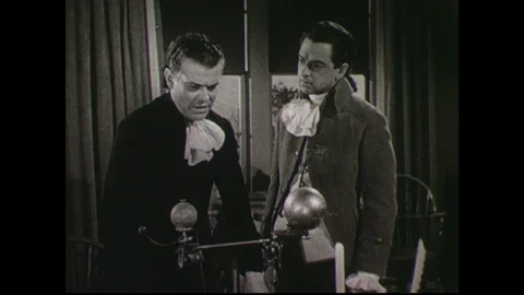 1940s: Two men stand in study, in front of desk with device on it, having a Stock Footage 90560873
