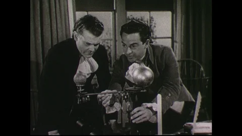 1940s: Two men stand in study, in front of desk with model orrery of universe on Stock Footage 90560878