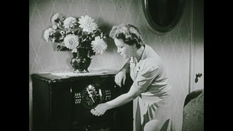 1940s: Woman turns knob on radio. Family sits at dining table and listens to Stock Footage
