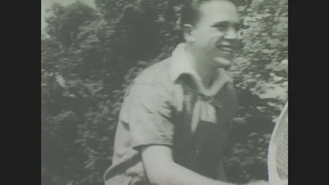 1940s: Young man smiles, holds racket. Young girl walks to tennis net, young man Stock Footage