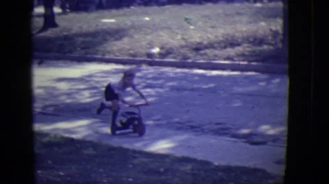 1946: cute caucasian blond kid riding scooter on sidewalk coming up to house Stock Footage
