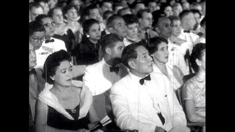 1950s: Black tie event, mostly Asian audience listens, people fan themselves, Stockbeeldmateriaal 89857184