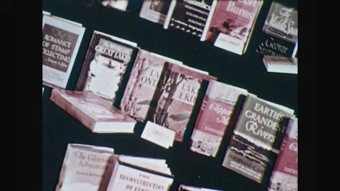 1950s: Books line up in window display. Book covers. Male students leave Vídeos de archivo 77740106