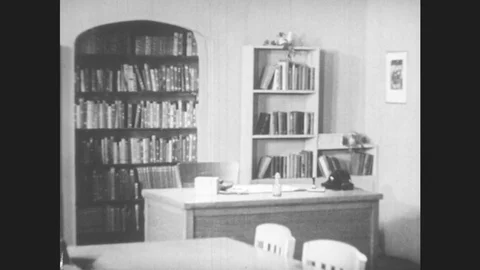 1950s: Books lined on shelves a desk and several tables with chairs. Teenagers Stock Footage