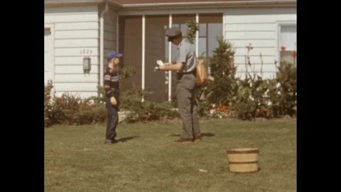 1950s: A boy digs in the front yard. A mailman walks, shuffling a stack of Vídeo Stock 260128445