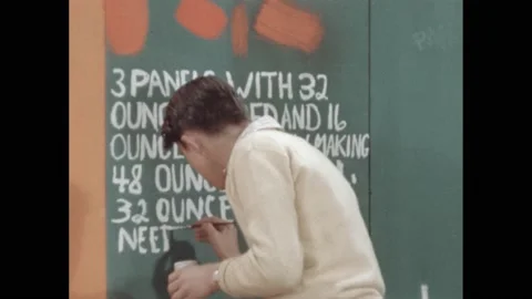 1950s: boy dips brush in jar and paints white letters on wall with math problem Vídeos de archivo 172030943