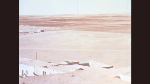 1950s: Boy in head scarf standing on clay roof of building in the desert points Stock Footage