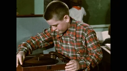 1950s: Boy opens lid of phonograph and adjusts knobs and needle. Teacher hands 스톡 동영상 169182959
