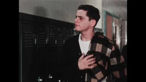 1950s: Boy puts coat and books into school locker while students pass in Stock Footage 284848500