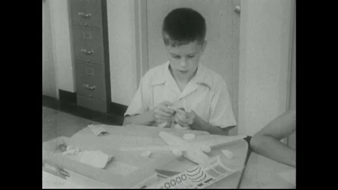 1950s: Boy puts model plane together / Hand puts tail on plane / Hands spin 動画素材 74618584