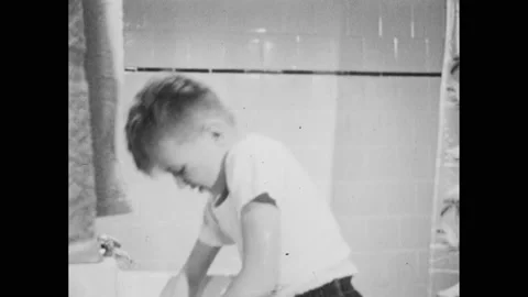 1950s: Boy rinses soapy hands off in sink. Boy drains sink. Billy wets washcloth Stock Footage 239107096