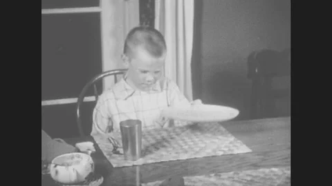 1950s: Boy sets empty plate on table and eats a piece of bread. Girl puts on Stock Footage 80123291