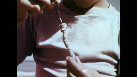 1950s: Boy strings stone with hole in center on wire containing similar stones. Video stock 84442422