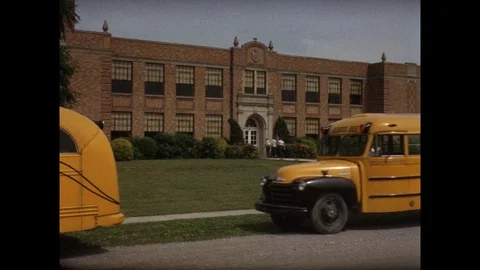 1950s: Buses pull up in front of school.  Teacher and students get off bus and Stock Footage 112430783