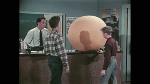 1950s: Classroom, teacher stands over lab table. Solar system model, balls, Stock Footage 221423917