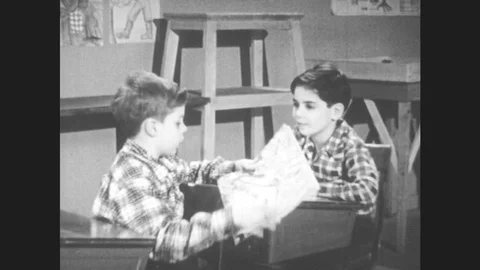 1950s: Classroom, two boys sit at desks, boy in front shows boy behind him his Stock Footage