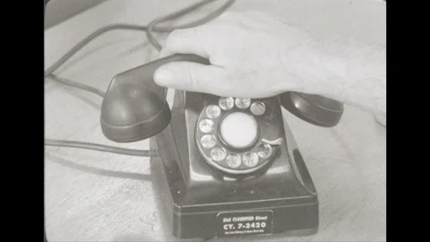1950s: Close up, hand picks up phone. People in office, man on phone, man Stock Footage