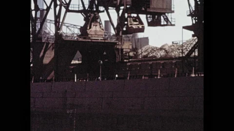 1950s: Crane lifting material from ship. Crane lowering beams into train car. Video stock 146798297