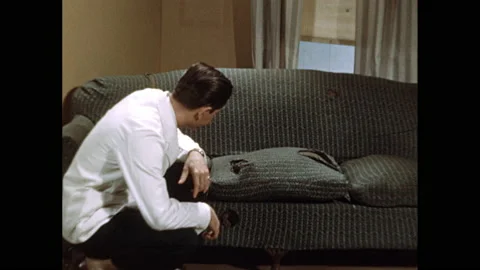 1950s: Doctor's office, lumpy worn out couch. Doctor kneels, examines rips in Stock Footage 140123566