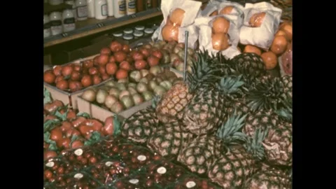 1950s: Fruits sit on display on grocery store table. Woman picks up bag of Stock Footage 273884454
