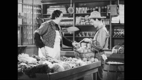 1950s: Grocer greets boy and takes tomato from basket. Boy and grocer talk over Stock Footage 143783891