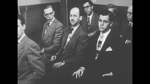 1950s: The group sits, a man from the group stands up and talks. Man stands, Stock Footage