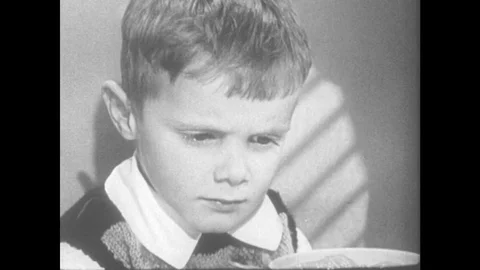 1950s: Grumpy boy at meal table. Boy makes angry face without speaking. Woman Video stock 78548645