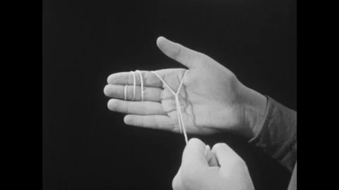 1950s: hand pulls string wrapped around other hand, breaks string, man talks, Stock Footage 127720109